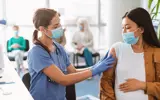 Pregnant Asian lady getting vaccinated, nurse applying adhesive bandage